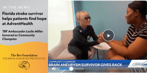 A smiling woman in scrubs holds hands with another woman wearing a headband, both seated and facing each other. The screen reads Brain aneurysm survivor gives back and highlights a story about a stroke survivor at AdventHealth.