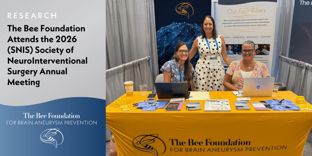 Three women smile at a conference booth for The Bee Foundation for Brain Aneurysm Prevention, with brochures, pens, and laptops displayed on a yellow tablecloth. A sign mentions attendance at the 2026 SNIS Annual Meeting.
