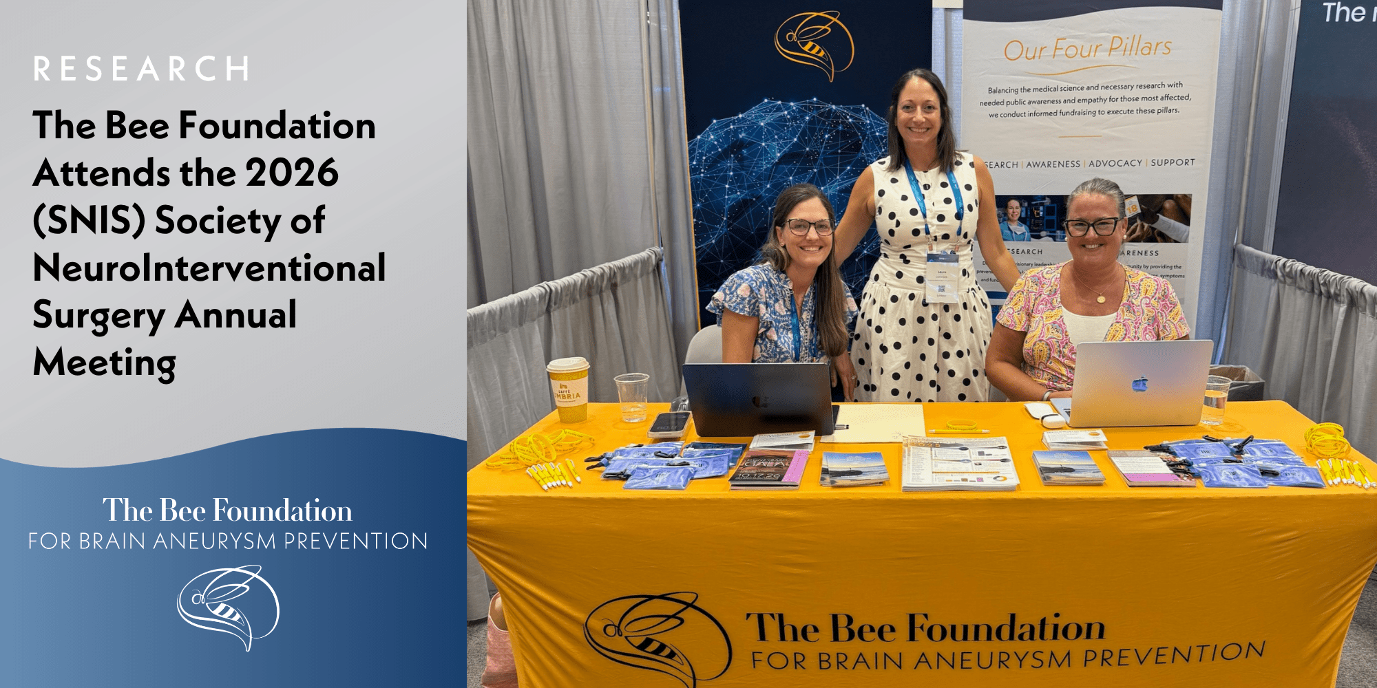 Three women smile at a conference booth for The Bee Foundation for Brain Aneurysm Prevention, with brochures, pens, and laptops displayed on a yellow tablecloth. A sign mentions attendance at the 2026 SNIS Annual Meeting.