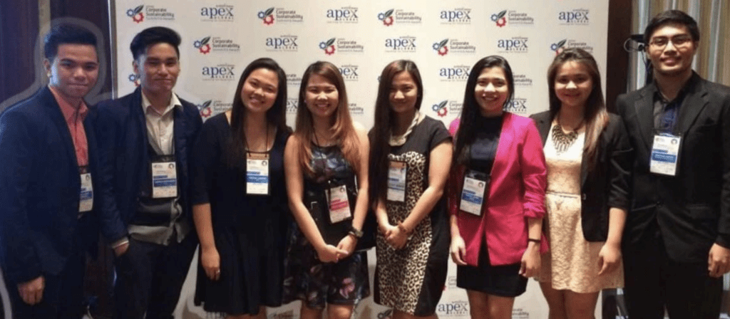 Eight people stand side by side, smiling at the camera, dressed in business attire with conference badges, in front of a branded event backdrop.