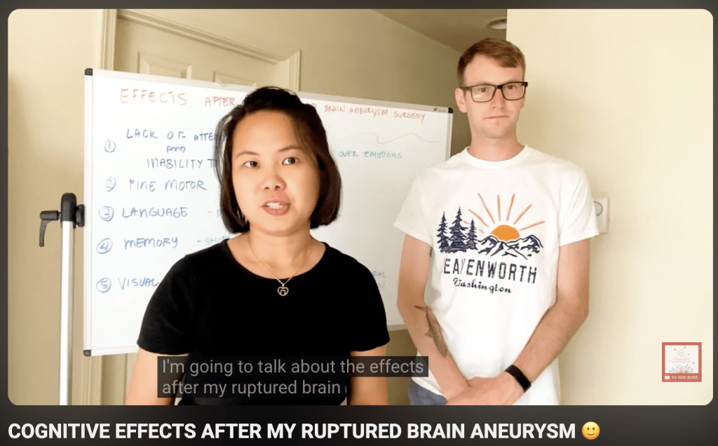 A woman speaks in front of a whiteboard labeled Effects after brain aneurysm surgery while a man stands beside her; subtitles read, Im going to talk about the effects after my ruptured brain..
